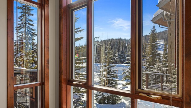 A window with a view of a snowy mountain landscape, including trees and a ski lift. - Bright, Ski-in/Ski-out Townhouse with A/C (Sun Peaks)