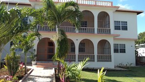 A two-story building with a balcony, arched windows, and a garden with various plants. - Apartment - Walk to the Beach (Lucea)