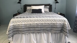 A neatly made bed with a patterned bedspread and pillows, two bedside lamps, a framed picture on the wall, and a small table with a lamp on the side. - Apartment - Walk to the Beach (Lucea)