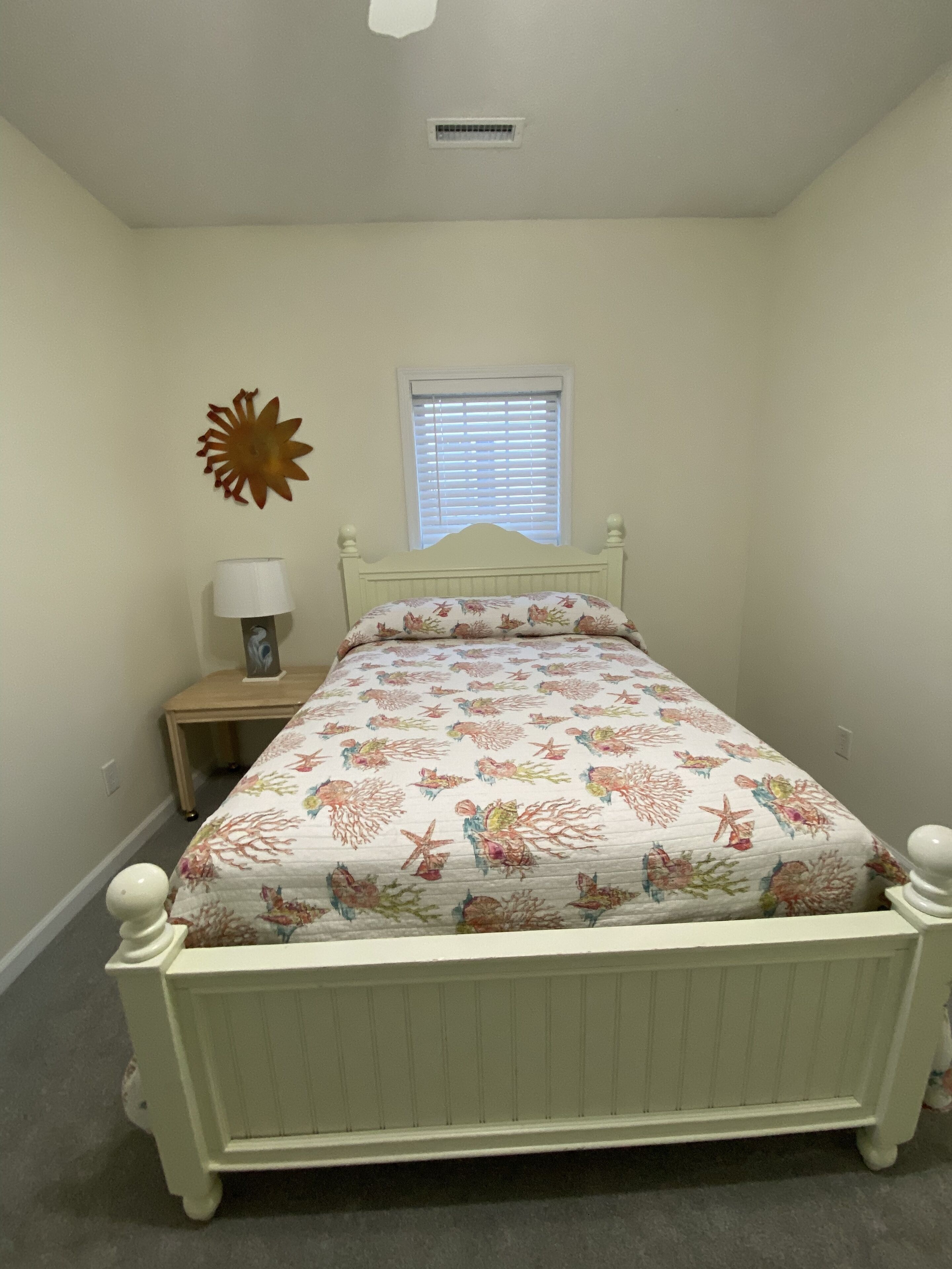 Une chambre à coucher avec un lit, une table de chevet, une lampe, un élément de décoration murale et une fenêtre.