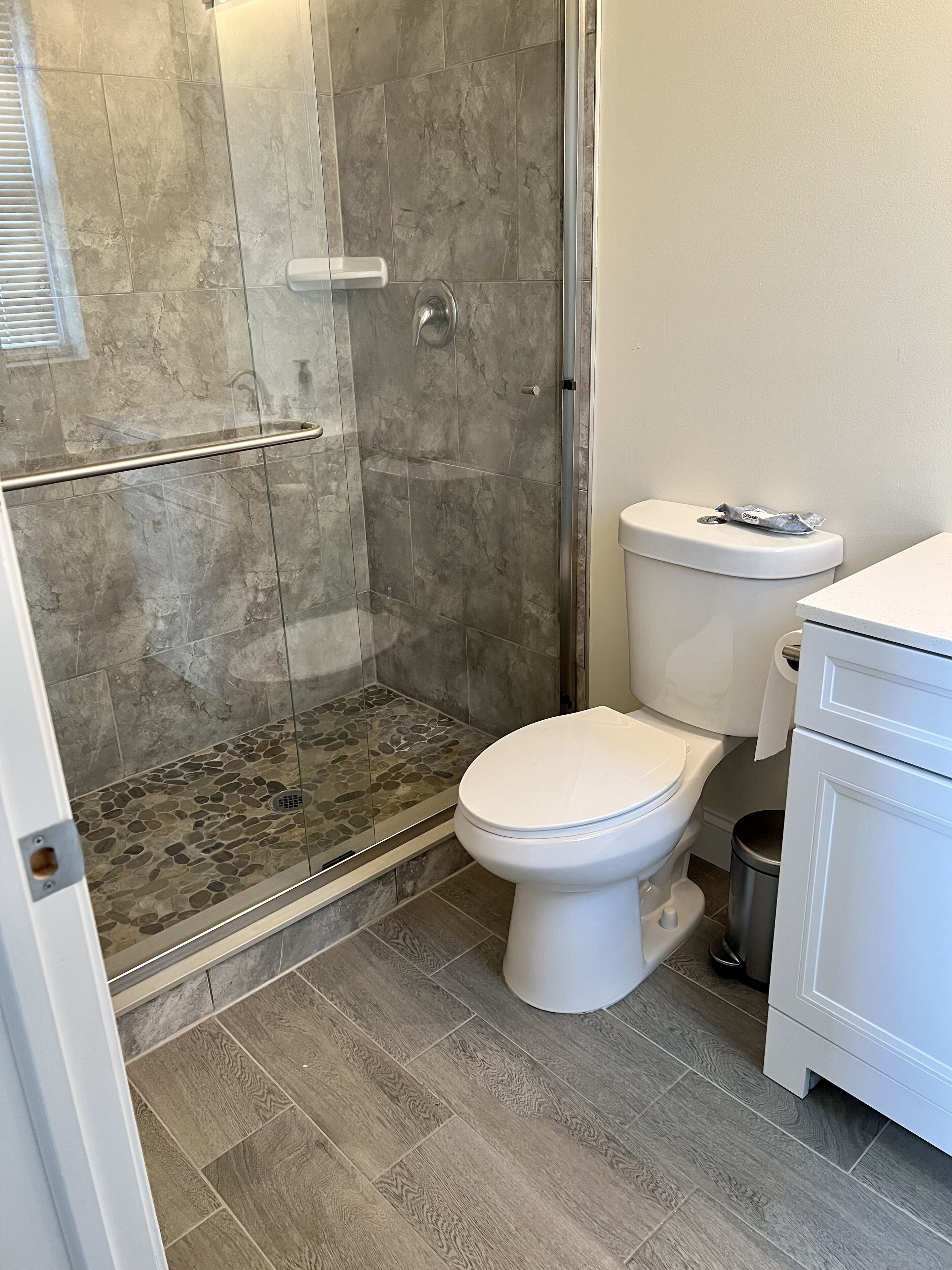 A bathroom with a shower, toilet, and a trash can.