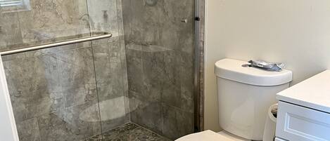 A bathroom with a shower, toilet, and a trash can.