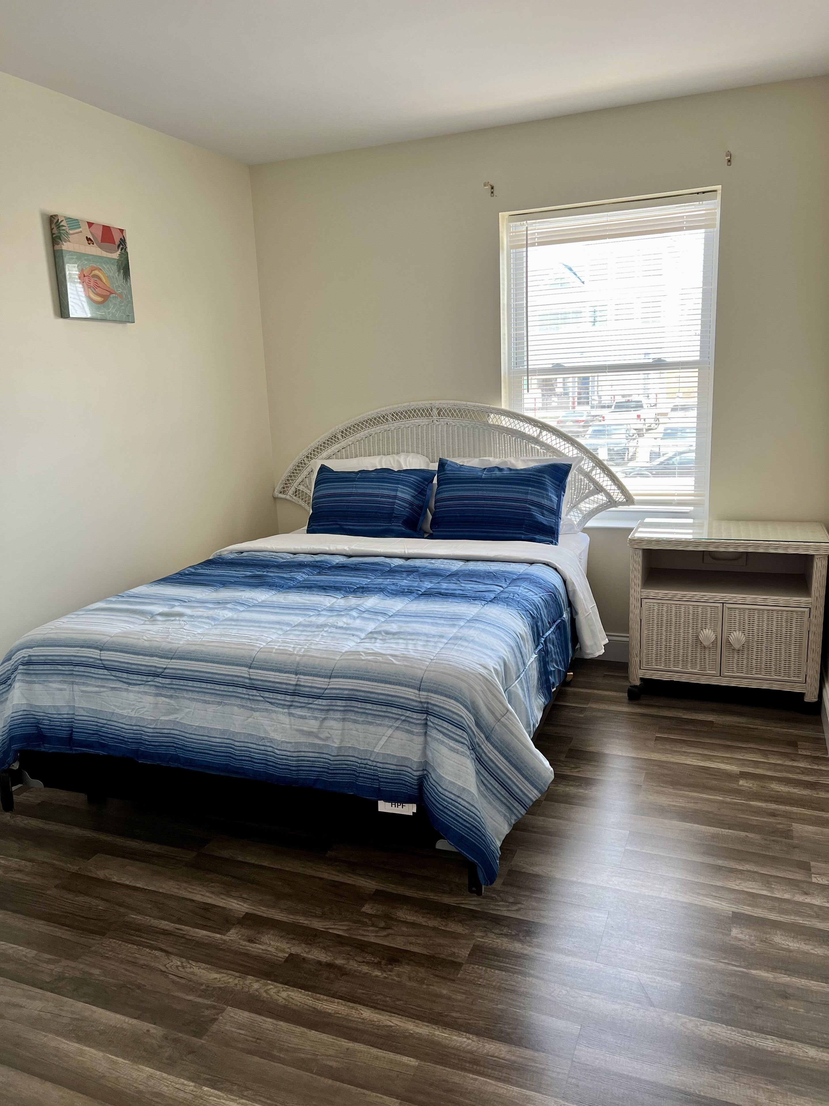 A bedroom with a bed, a window, a nightstand, and a wall decoration.