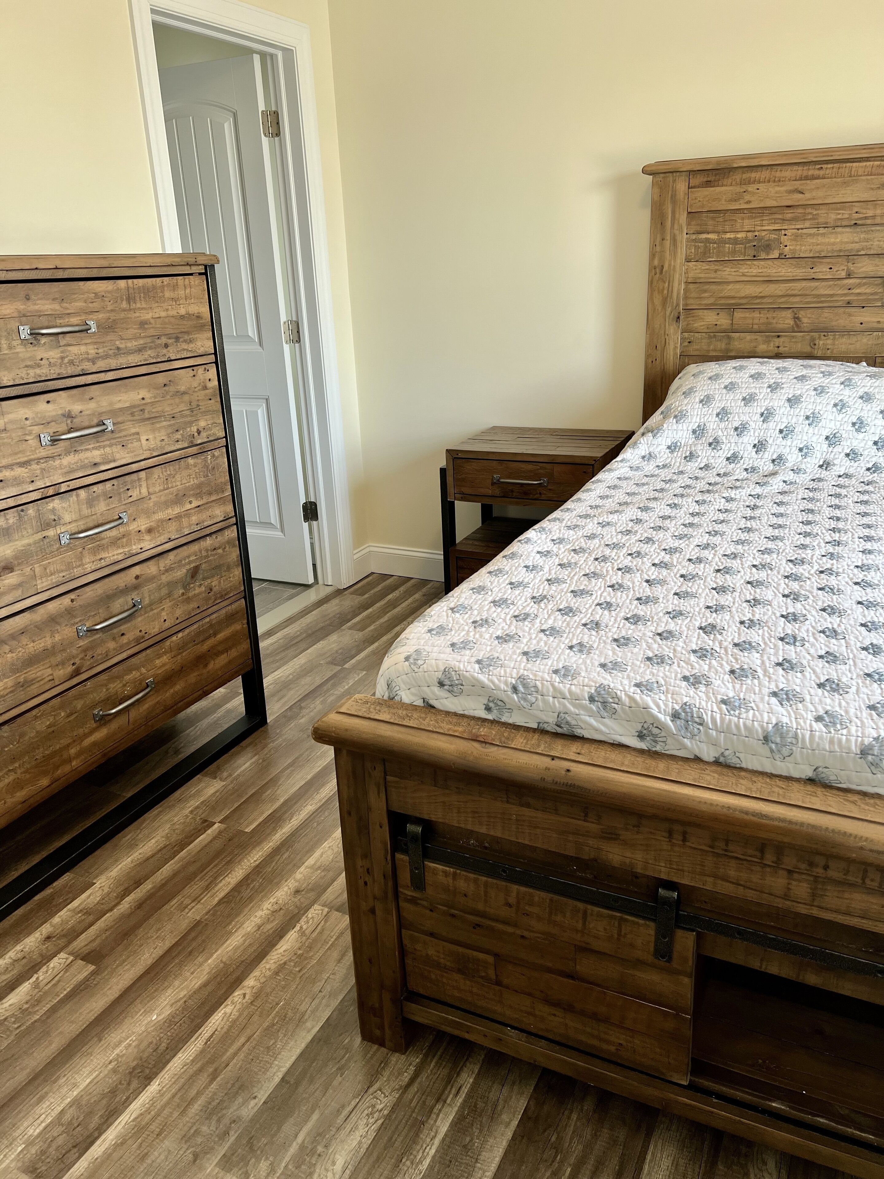 A bedroom with a wooden bed, a dresser with multiple drawers, and a small table.