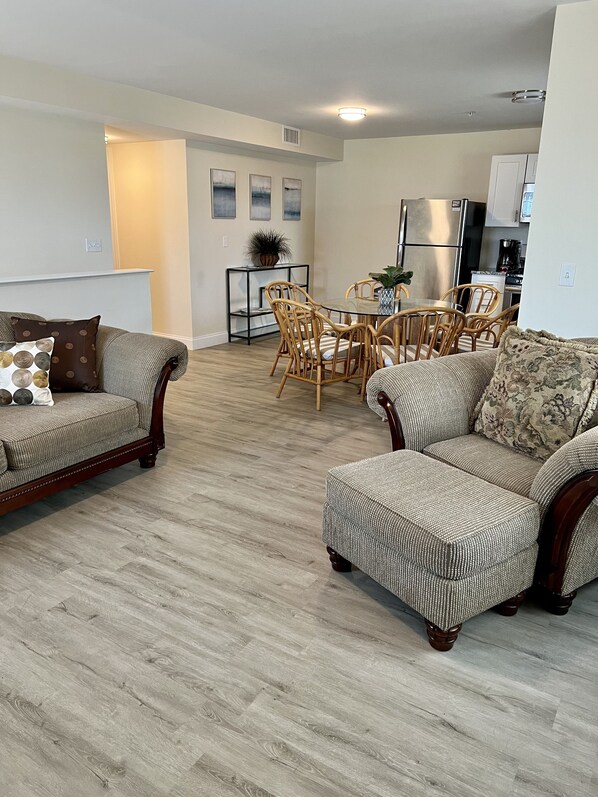 A living room with two sofas, a dining table with chairs, and a kitchen area in the background. - Spacious 4BR Coastal Condo • Steps to Beach & Boardwalk • Parking + Badges (Seaside Heights)