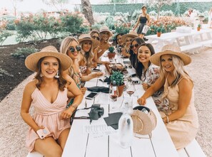 Un grupo de personas sentadas en una mesa blanca al aire libre, con un jardín de fondo.