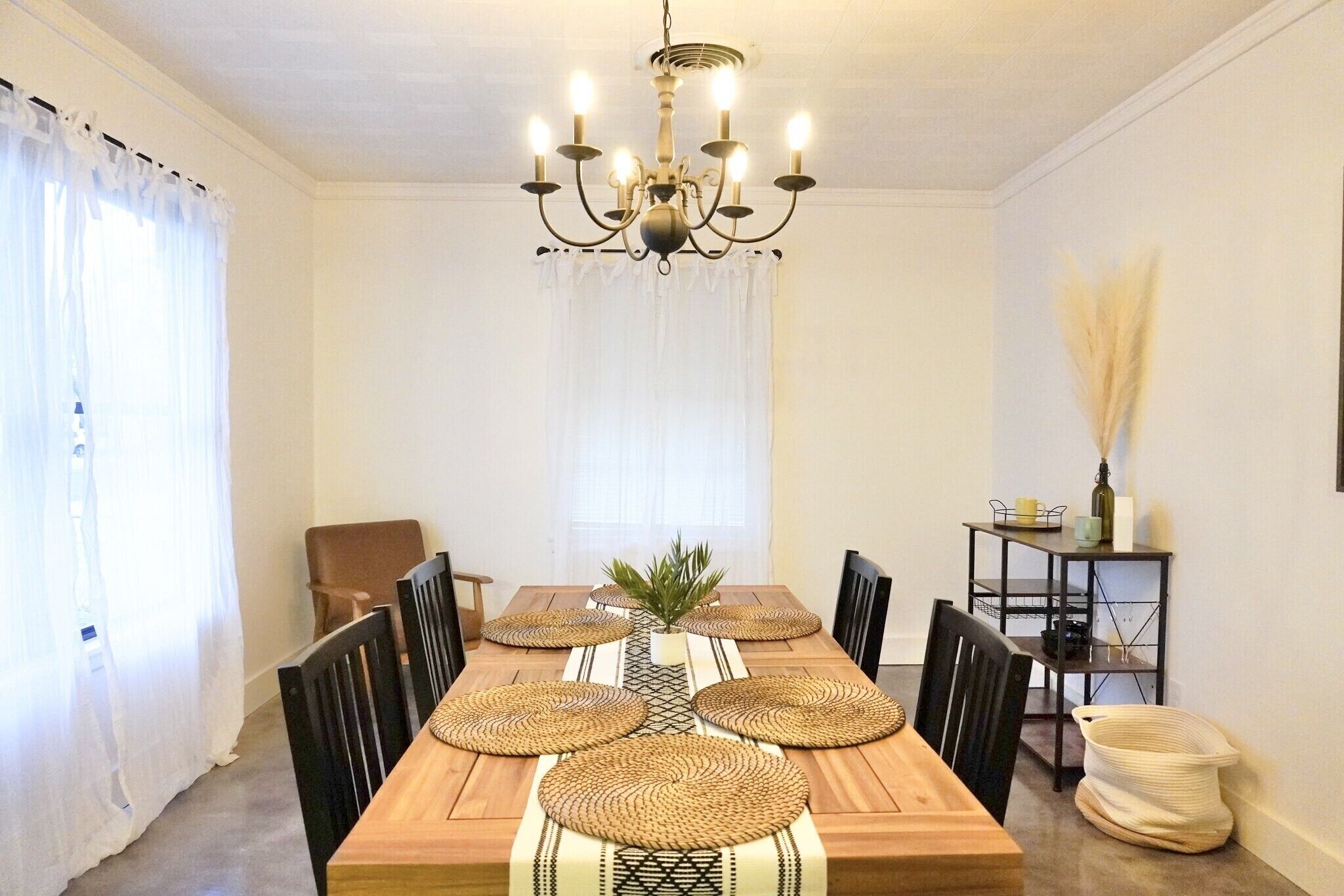 Ein Esszimmer mit einem Holztisch, schwarzen Stühlen, einer Chandelüster und einem kleinen Beistelltisch mit einer Vase.