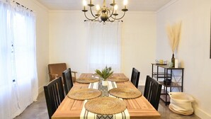 Comedor con mesa de madera, sillas negras, una araña y una mesita auxiliar con un jarrón.