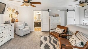 Un dormitorio moderno con cama, dos sillas, cómoda y ventilador de techo.