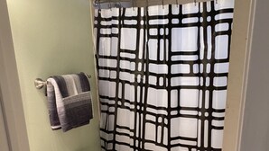 Ein Badezimmer mit Toilette, Waschbecken, einem Handtuch an der Wand und einer Duschvorhang mit geometrischem Muster.