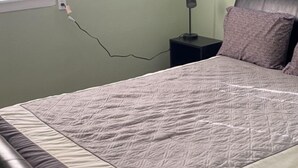 Ein Schlafzimmer mit einem Bett, einem Nachttisch, einer Lampe und einem Fenster.