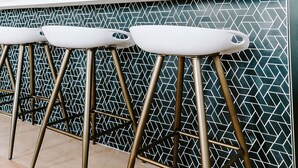 A modern kitchen with a white countertop, two stools, and a patterned backsplash. - Modern Shipping Container Guest House w/ City Views (Denver)