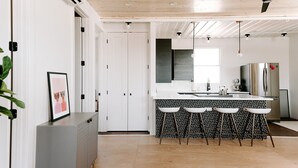 A modern kitchen with a central island, bar stools, a refrigerator, and a window. - Modern Shipping Container Guest House w/ City Views (Denver)