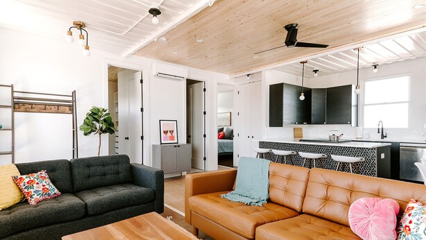 A modern living room with a sofa, coffee table, and a kitchen area with a bar. - Modern Shipping Container Guest House w/ City Views (Denver)
