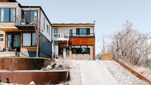 A modern two-story house with a garage, a balcony, and a small outdoor seating area. - Modern Shipping Container Guest House w/ City Views (Denver)