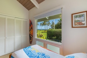Une chambre à coucher avec un lit, une fenêtre donnant sur des palmiers et une plage, et un placard avec des volets blancs.