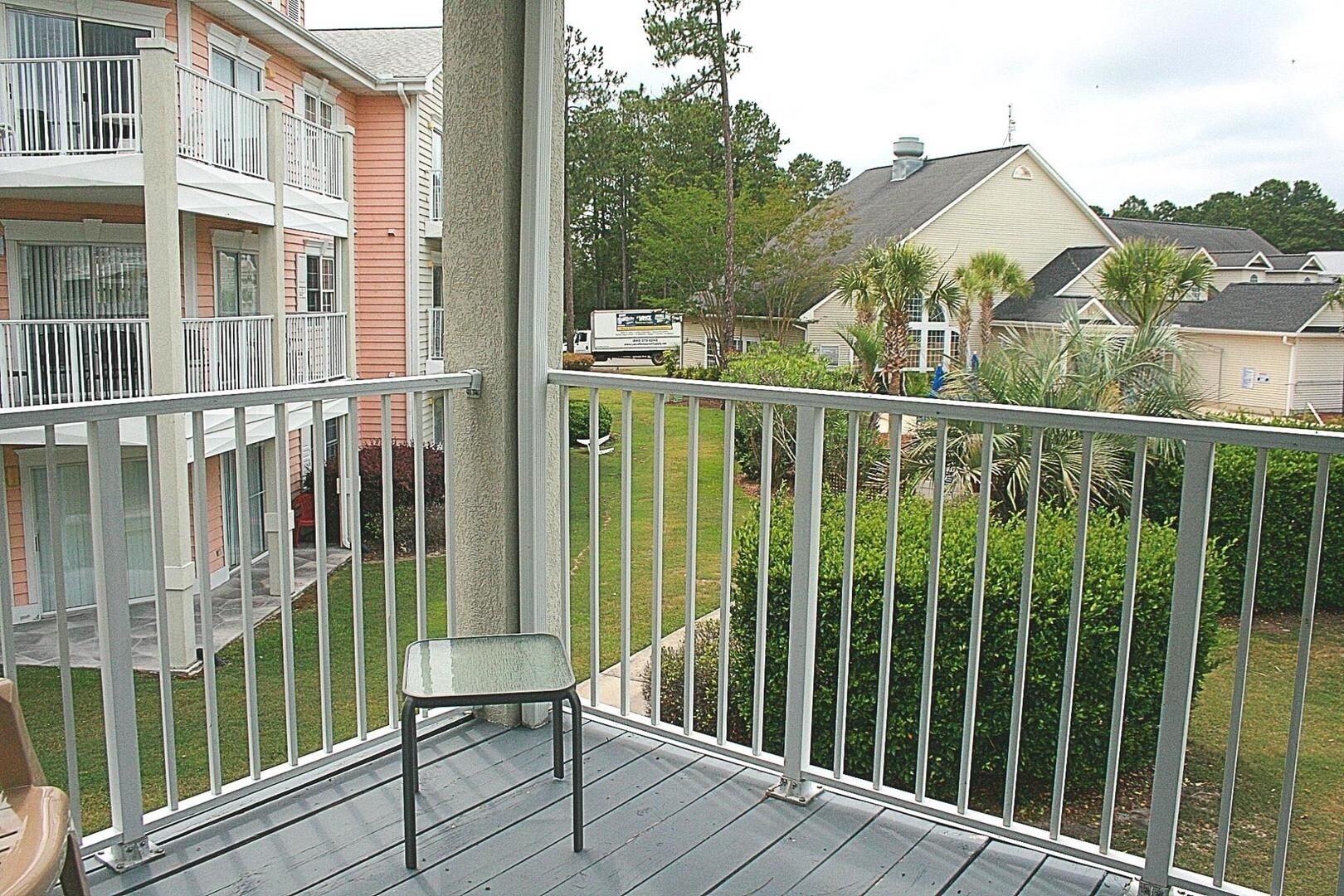 A balcony with a metal railing, a chair, and a view of neighboring houses and greenery.