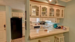 A kitchen with white cabinets, a black refrigerator, a stove, and a microwave. There are two stools and a countertop with various items.