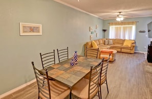 Un coin repas avec une table dressée pour quatre personnes, entourée de chaises en métal. Un canapé et une petite table se trouvent à l’arrière-plan.