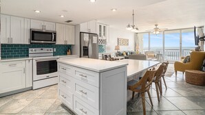 A modern kitchen with white cabinets, a large island, and a dining area with a view.