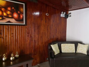 A room with wooden paneling, a dark brown leather sofa with patterned cushions, a framed picture of onions, and a small table with decorative pineapple-shaped vases.