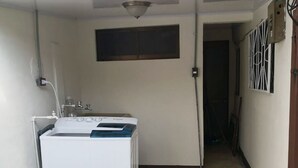 A laundry room with a washing machine, a small window, and a door leading to another room. - Flor Tica House (Quepos)