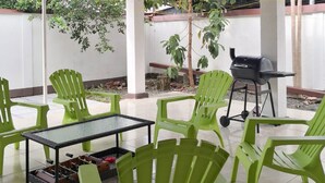 A patio area with green plastic chairs, a table with a foosball table, and a barbecue grill. - Flor Tica House (Quepos)