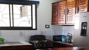 A kitchen with wooden cabinets, a gas stove, a refrigerator, and a window with a metal grill. - Flor Tica House (Quepos)