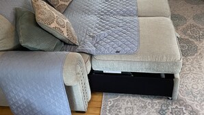 Un canapé modulable avec des coussins à motifs, un plaid assorti et un tapis à motifs, dans une pièce dotée d’un plancher en bois et d’une fenêtre avec des stores.