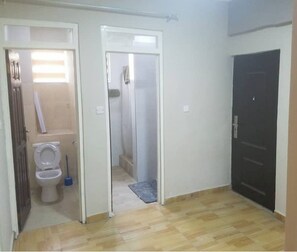 A room with a wooden floor, a toilet, a shower, and a door.