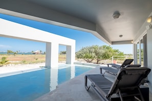 Un área de piscina moderna al aire libre con sillones de descanso, una vista despejada del mar y jardines bien cuidados.