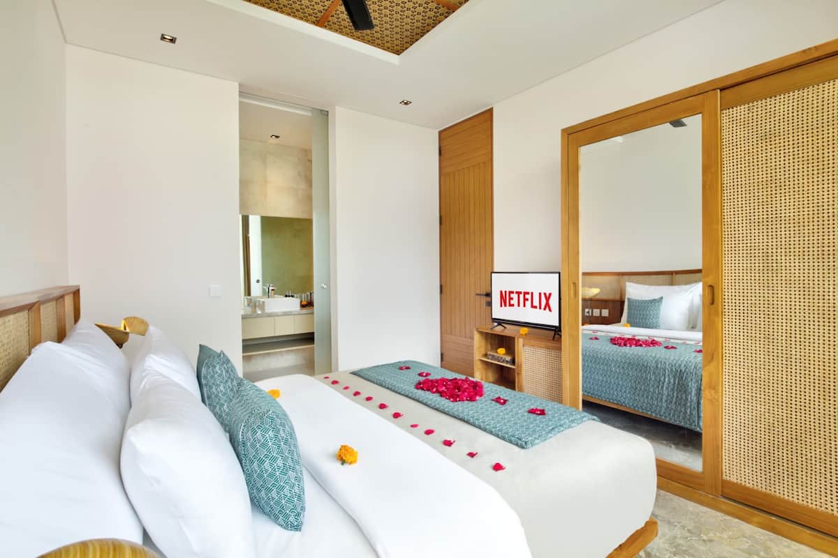A hotel room with a bed, a television displaying 'NETFLIX', and a bathroom visible through an open door.