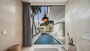 Un baño moderno con una bañera grande, un ventanal pequeño y vistas a una piscina.
