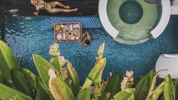 A swimming pool with a floating tray of food, a lounge chair, and tropical plants.
