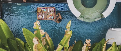 A swimming pool with a floating tray of food, a lounge chair, and tropical plants.