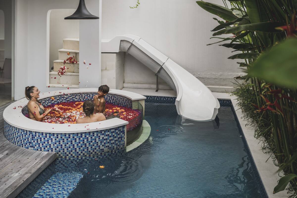 A pool with a slide, a hot tub with flower petals, and a staircase.