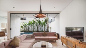 Un salon moderne avec un canapé, une table basse, un téléviseur et une vue sur une piscine et des plantes.