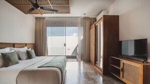 Une chambre d’hôtel équipée d’un lit, d’une télévision, d’un ventilateur de plafond et d’une porte-fenêtre coulissante donnant sur un balcon.