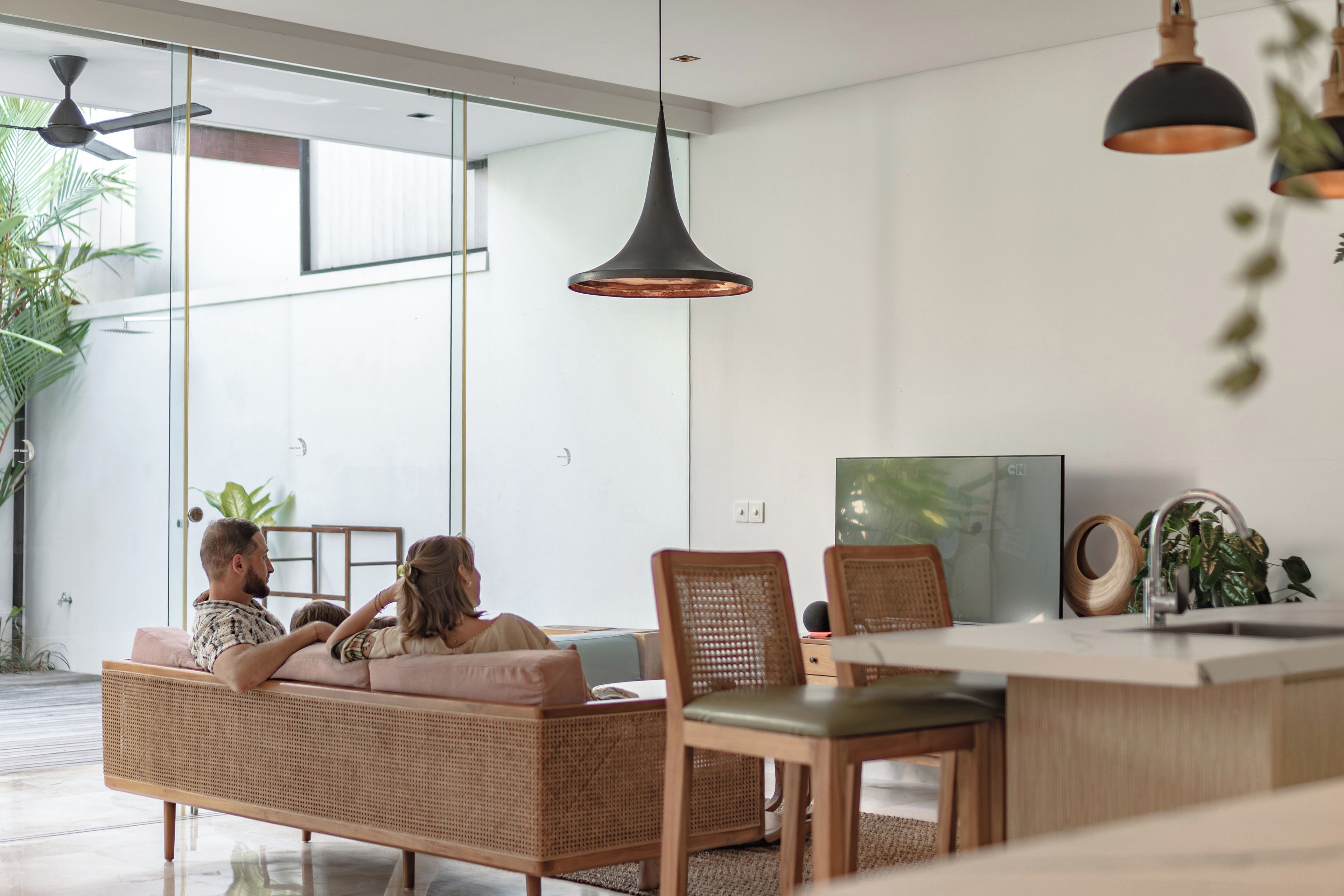 A modern living space with a glass partition, wicker furniture, and pendant lighting.