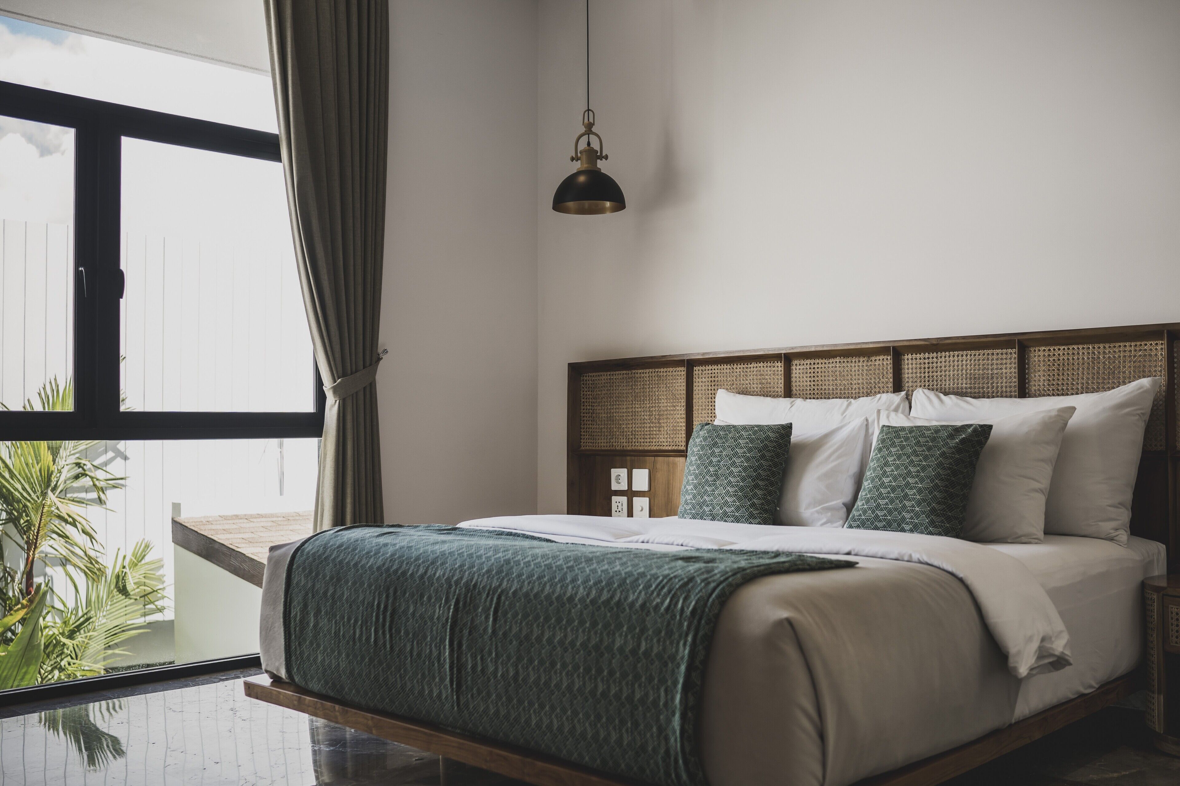 A modern bedroom with a large window, a bed with white and green bedding, and a hanging lamp.