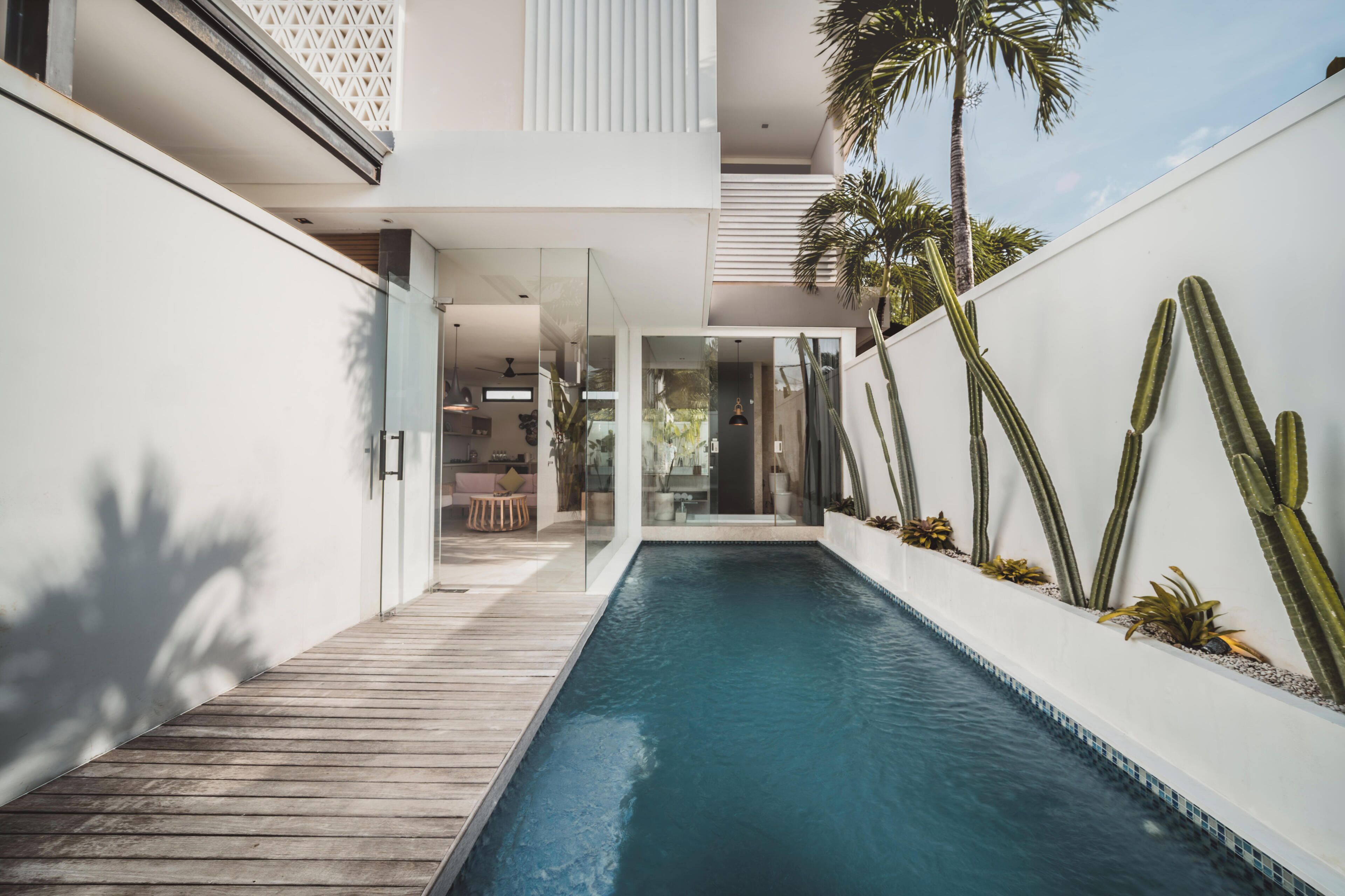 A modern pool area with a wooden deck, glass walls, and cacti.