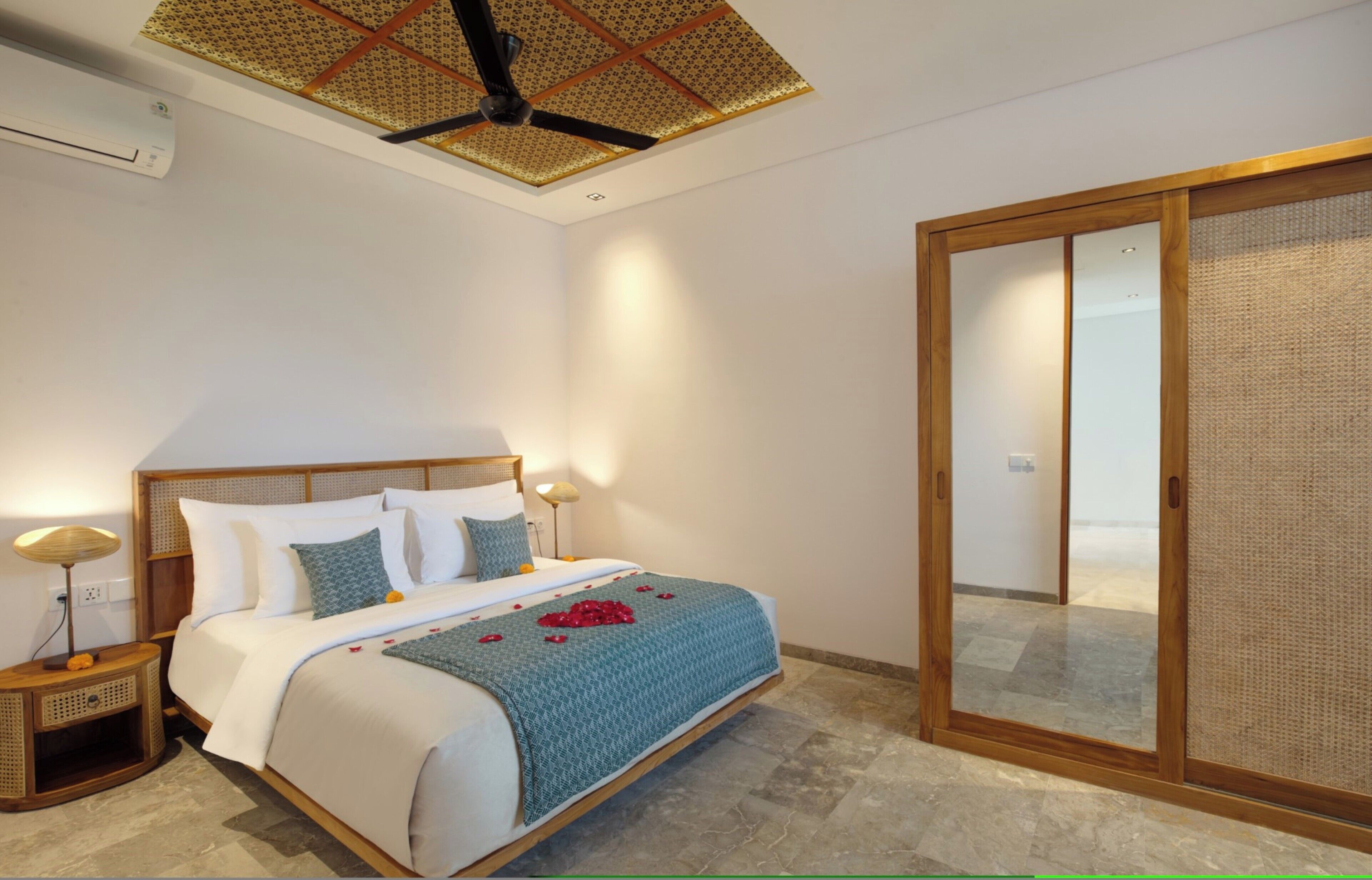 A bedroom with a bed, bedside lamps, a ceiling fan, and a sliding glass door.