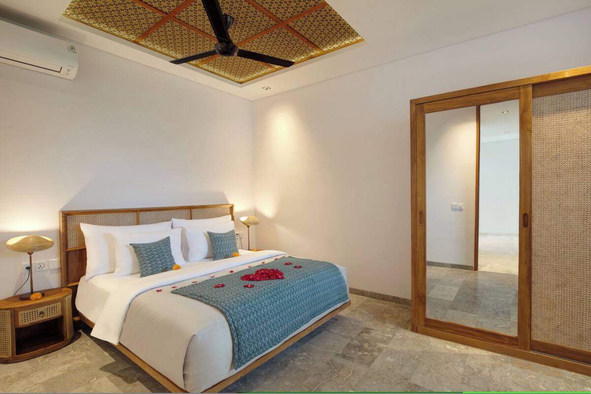 A bedroom with a bed, bedside lamps, a ceiling fan, and a sliding glass door.