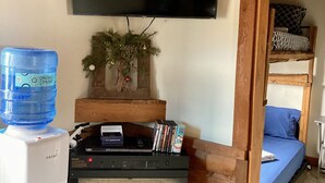 A cozy room with a fireplace, a water dispenser, a flat-screen TV, and a bed with a blue blanket. - Tiny Cabin, pet-friendly Mins from Cook Forest & Allegheny National Forest! (Marienville)