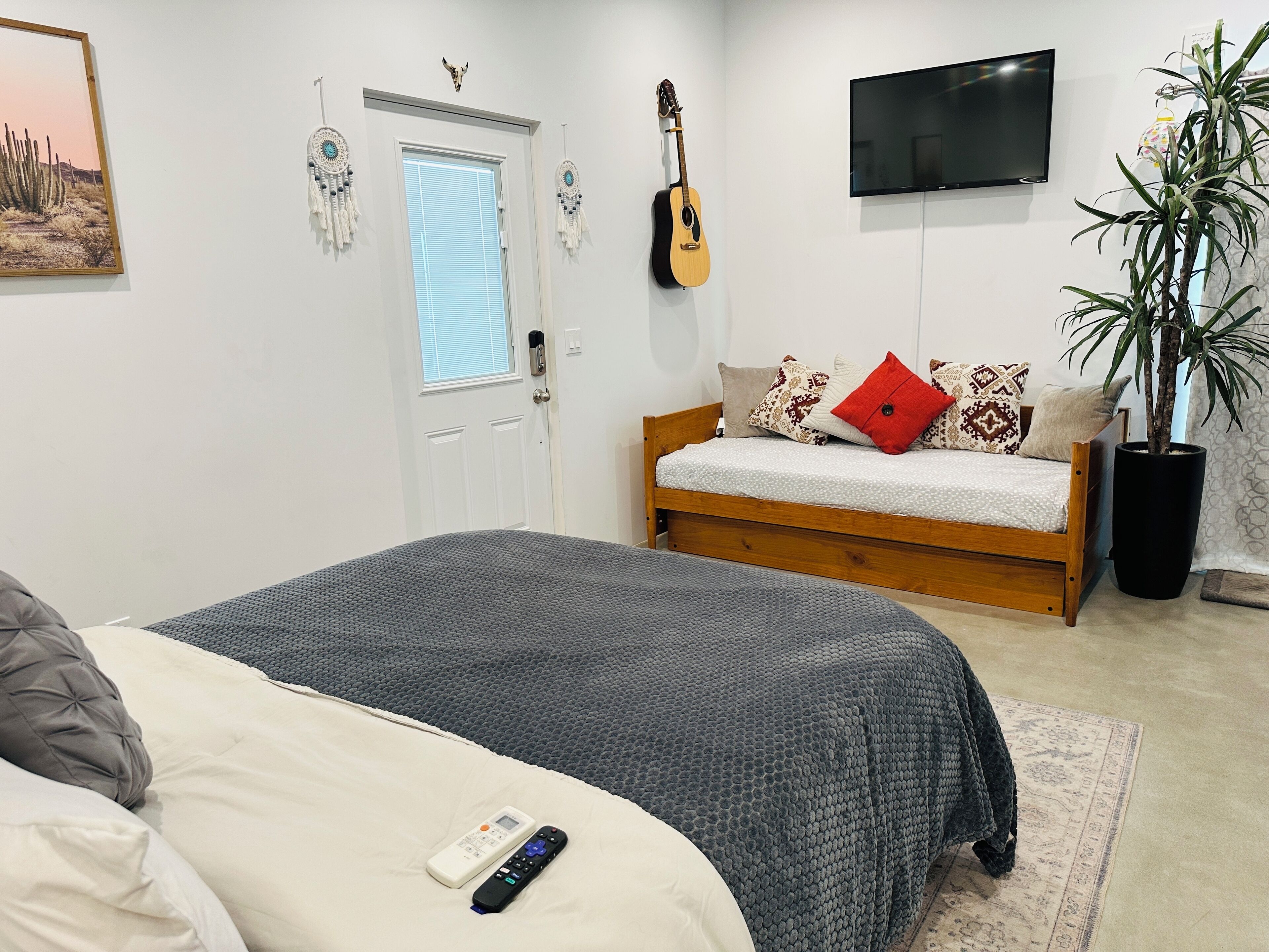 A bedroom with a bed, a guitar, a TV, and a potted plant.