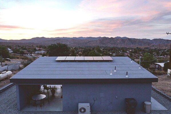 Un toit équipé de panneaux solaires, un petit espace extérieur aménagé avec des sièges, et une vue sur un paysage désertique avec des montagnes en arrière-plan.