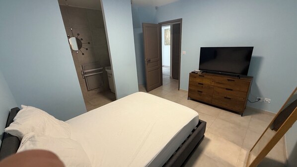 A bedroom with a bed, a dresser, a television, and a bathroom visible through an open door.