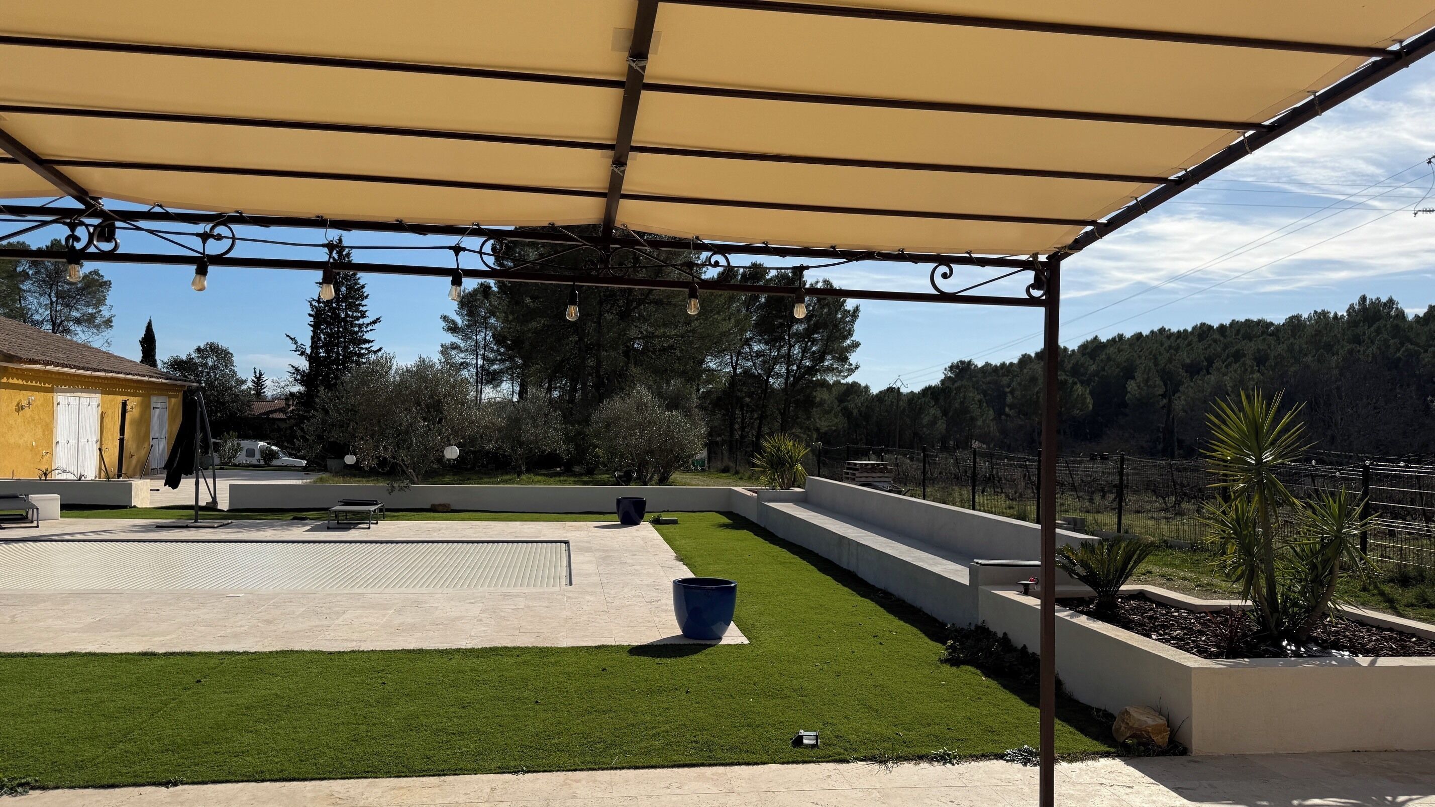 A covered outdoor area with a patio, a lawn, and a fence.