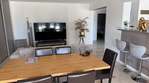 Un salon moderne avec une table à manger en bois, des sièges confortables, un téléviseur à écran plat et une plante en pot.