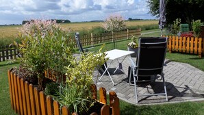 Eine Terrasse im Freien mit Tisch und Stühlen, umgeben von Pflanzen und einem Holzzaun.